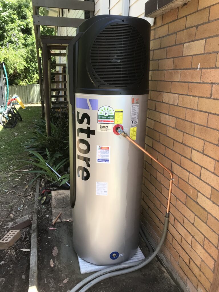 iSTORE HEAT PUMPS » iSTORE HEAT PUMPS An outdoor silver and black iStore air-to-energy heat pump system installed against white horizontal siding.