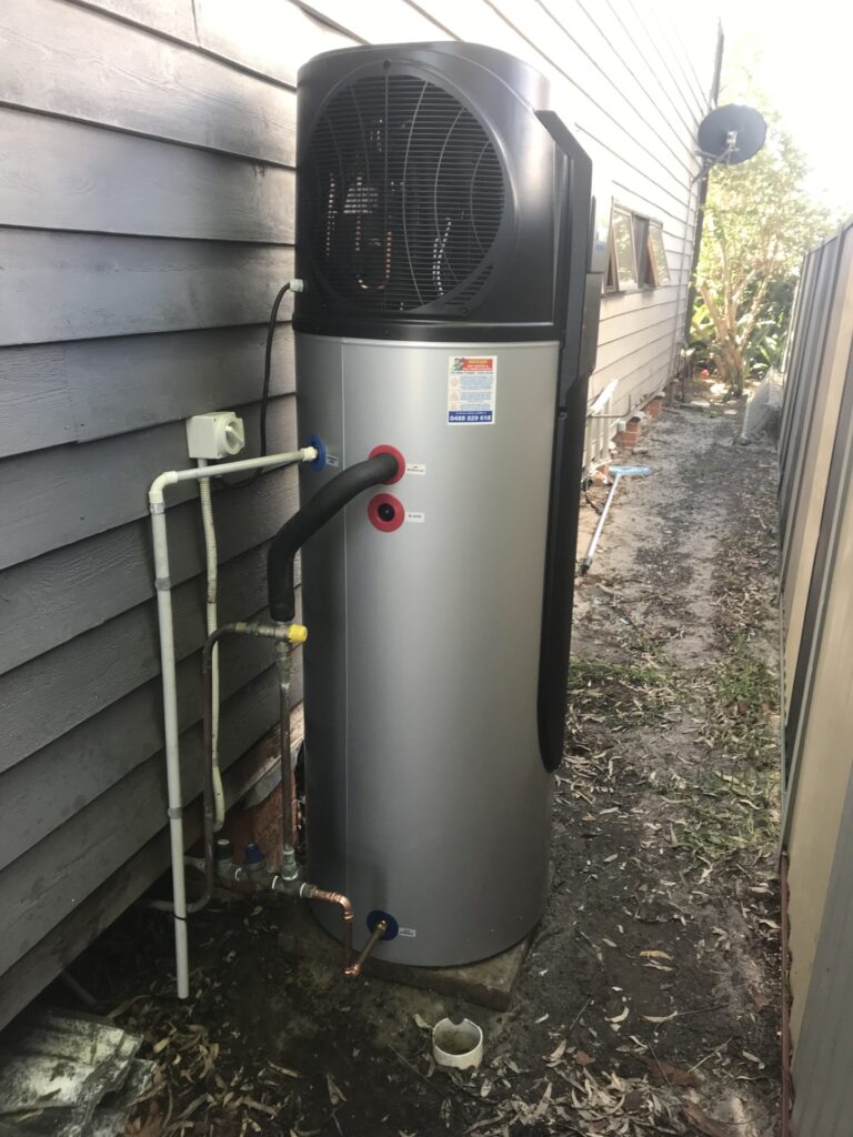 iSTORE HEAT PUMPS » iSTORE HEAT PUMPS An outdoor silver and black iStore air-to-energy heat pump system installed against white horizontal siding.