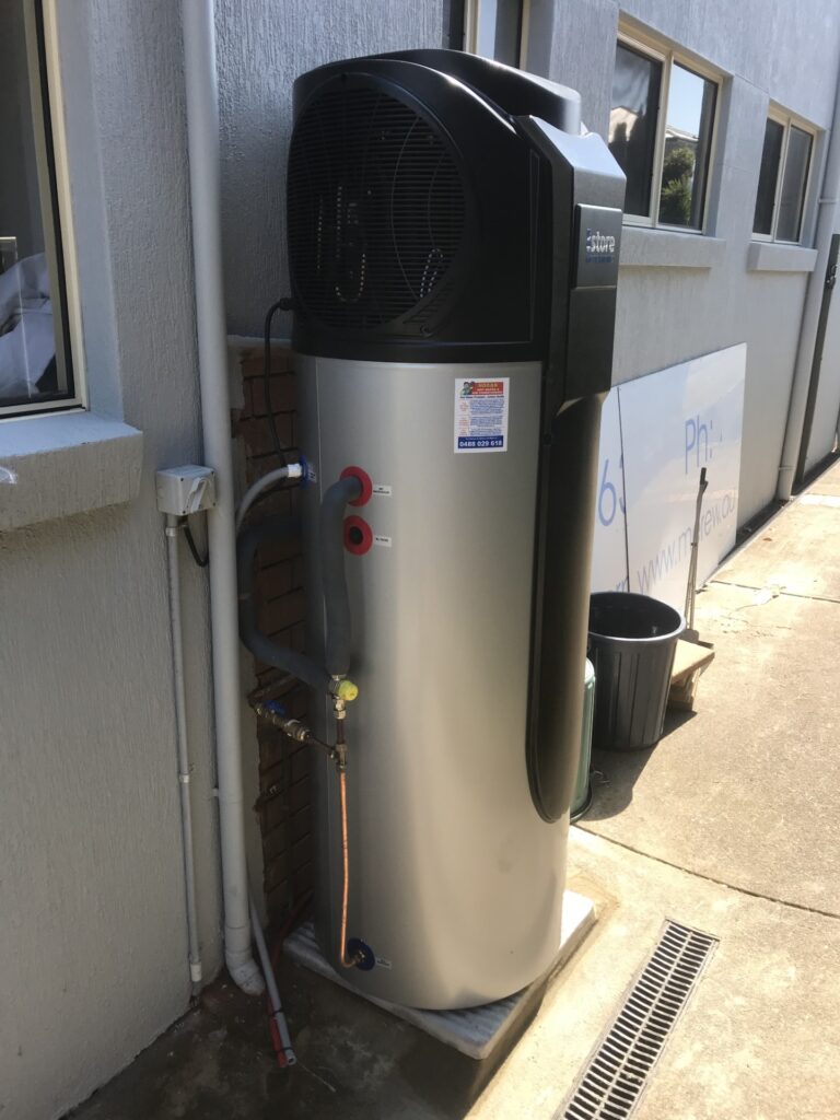 iSTORE HEAT PUMPS » iSTORE HEAT PUMPS An outdoor silver and black iStore air-to-energy heat pump system installed against white horizontal siding.