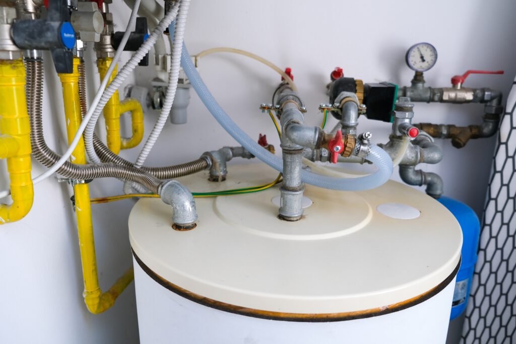 Hot Water Installation and Maintenance Phegans Bay » Hot Water A plumbing, metal pipes, yellow gas lines, flexible hoses, and valves connected to the top of a white domestic hot water storage tank.
