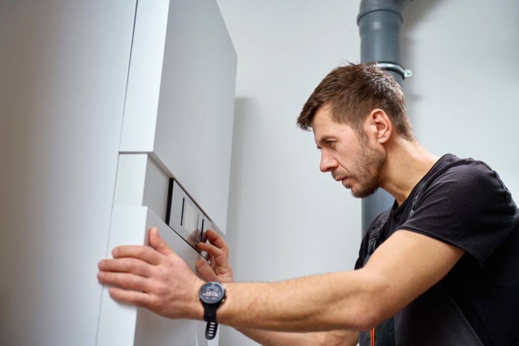 A technician in a black t-shirt adjusts the control panel of a modern heat pump system in Umina beach
