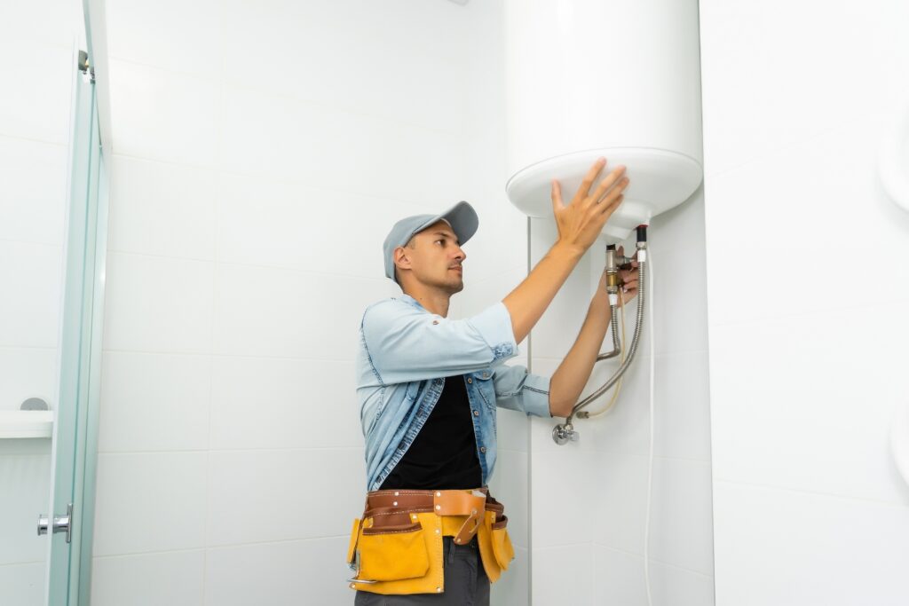 A technician in a tool belt installs a white cylindrical water heater mounted in Umina Beach