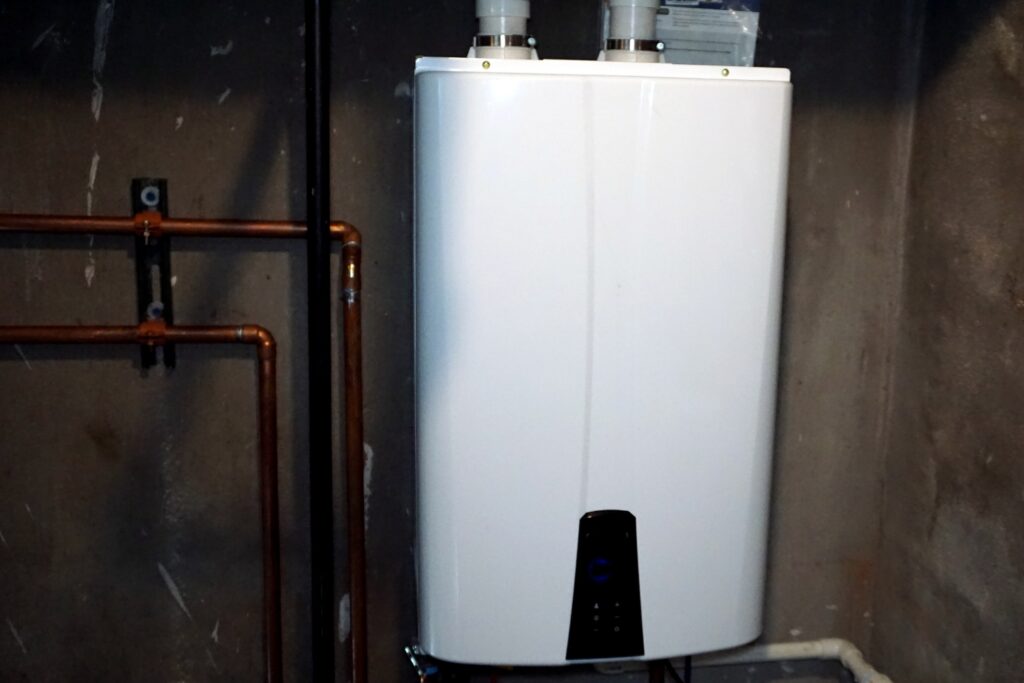 Hot Water Installation and Maintenance in Forresters Beach » Hot Water A modern white tankless water heater or heat pump control unit mounted on a concrete wall next to copper plumbing pipes.