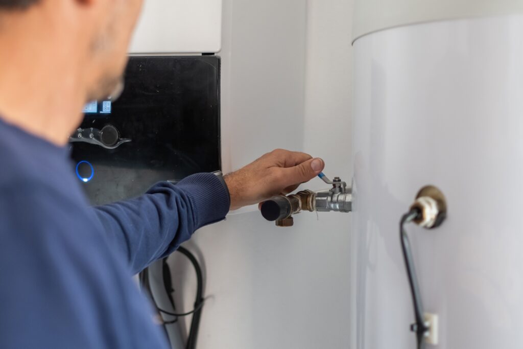 Hot Water Installation and Maintenance in Erina Heights » Hot Water A technician adjusting a valve lever on a pipe connected to a large white water storage tank.