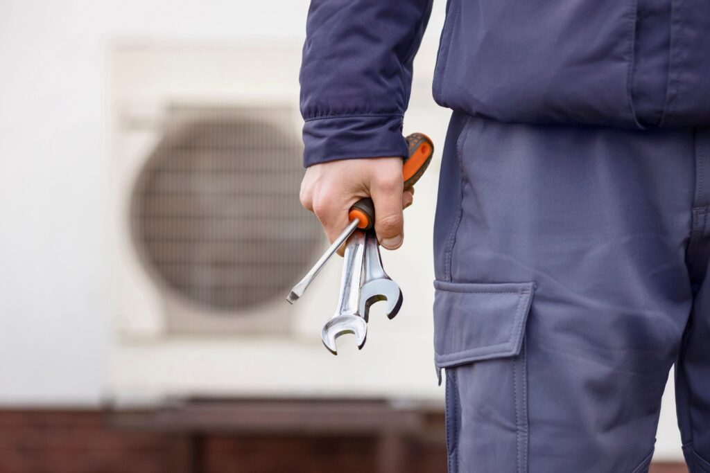 Hot Water Installation and Maintenance in Metford » Hot Water A technician in blue workwear holding a screwdriver and two metal wrenches.