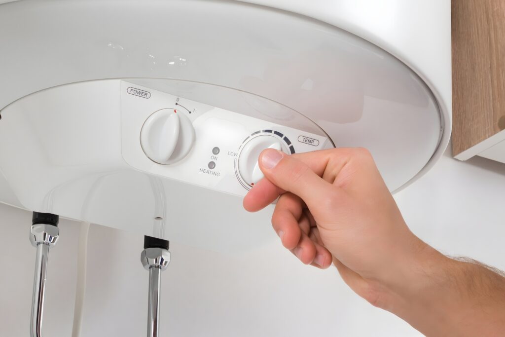 Hot Water Installation and Maintenance in East Maitland » Hot Water A close-up view of a person's hand turning a white temperature dial on the control panel of a wall-mounted hot water system.