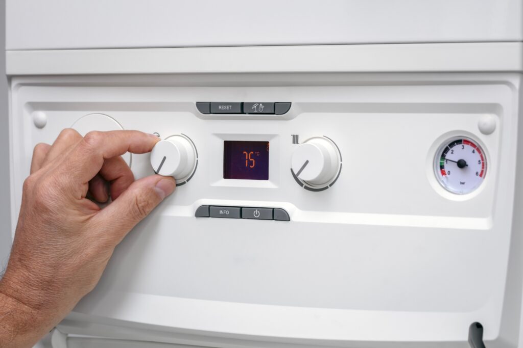 A hand adjusting the dial on a white water heater control panel, which displays a digital temperature of 75°C.