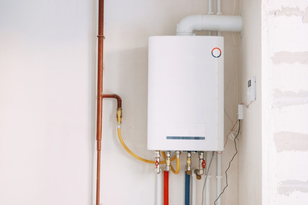 Hot Water Installation and Maintenance in Metford » Hot Water A white tankless water heater or boiler mounted on a wall with various colored pipes and valves connected at the bottom.