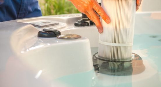 Hot Water Installation and Maintenance Lisarow A close-up view of a person's hands installing or removing a cylindrical, pleated white cartridge filter.
