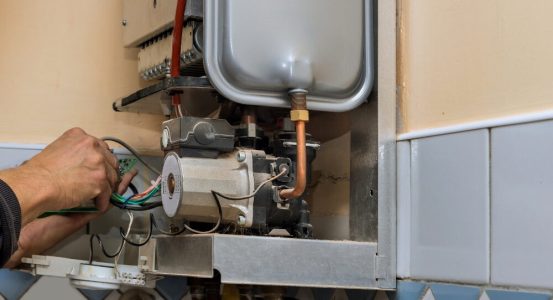Hot Water Installation and Maintenance Narara A technician's hands repairing the internal electrical wiring and circuit board panel of an opened wall-mounted gas boiler system.
