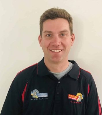 Photo 8-7-19, 3 09 31 pm A head-and-shoulders portrait of a smiling man wearing a black polo shirt with red trim