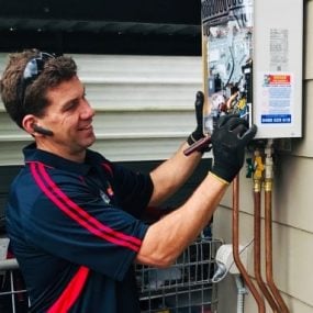 img3 A technician in a dark blue polo shirt with red stripes wearing black gloves while inspecting the internal components of a wall-mounted continuous flow hot water heater.
