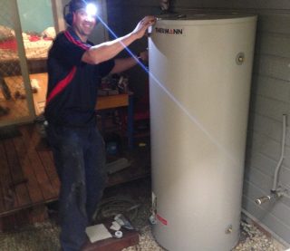 mk headlamp A smiling technician wearing a headlamp and earmuffs stands next to a tall, cream-coloured Thermann hot water storage tank